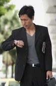Businessman holding briefcase, looking at watch, frowning - Asia Images Group