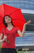 Woman with red umbrella, looking up, frowning - Asia Images Group