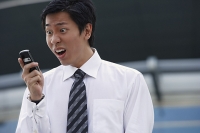Businessman looking at mobile phone, making a face - Asia Images Group