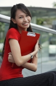 Young woman smiling at camera, hugging folder - Asia Images Group