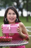 Woman sitting at outdoor cafe, holding pink gift, looking up - Asia Images Group