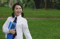 Young woman in school uniform, standing in park, looking away - Asia Images Group
