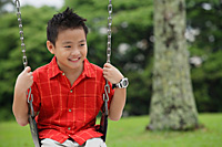 Boy in red shirt sitting on swing, smiling - Asia Images Group