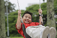 Boy on playground swing, smiling, looking away - Asia Images Group