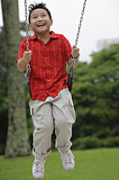 Boy on playground swing, smiling - Asia Images Group