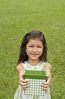 Girl standing on grass, holding gift box towards camera - Asia Images Group