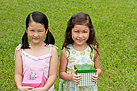 Two girls holding gift boxes, standing side by side, smiling at camera - Asia Images Group