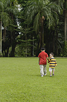 Two brothers walking in park, one looking over shoulder - Asia Images Group