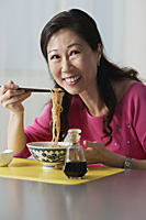 Mature woman eating a bowl of noodles - Asia Images Group