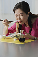 Mature woman eating a bowl of noodles, eyes closed - Asia Images Group