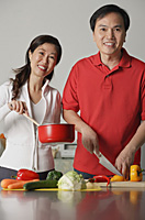 Mature couple in kitchen, preparing a meal together, smiling at camera - Asia Images Group