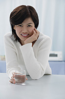 Woman leaning in table, holding glass, hand on chin, portrait - Asia Images Group