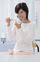 Woman in kitchen, holding bowl and chopsticks - Asia Images Group
