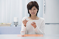 Woman in kitchen, eating with chopsticks, looking at camera - Asia Images Group