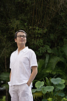 Man in white shirt and pants, standing in garden - Asia Images Group