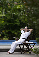 Mature man sitting outdoors, hands behind head, looking up - Asia Images Group