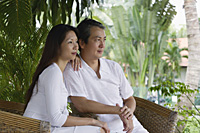 Couple sitting on rattan chairs, looking away - Asia Images Group