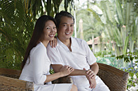 Couple sitting on rattan chairs, looking at camera, smiling - Asia Images Group