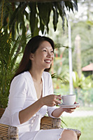 Woman sitting on patio, holding cup and saucer - Asia Images Group