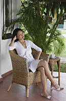 Woman sitting on rattan chair in patio, contemplative expression - Asia Images Group