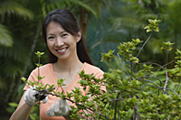 Woman in garden, pruning plants, smiling at camera - Asia Images Group