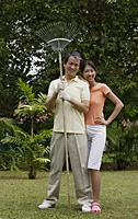 Couple standing side by side in garden, man holding garden rake - Asia Images Group