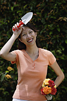 Woman holding trowel and bouquet of flowers, wiping her brow - Asia Images Group