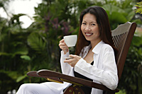 Woman sitting outdoors, having a cup of tea, smiling at camera - Asia Images Group