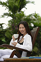 Woman sitting outdoors, drinking from cup - Asia Images Group
