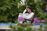 Woman sitting outdoors, hand on head, smiling at camera - Asia Images Group