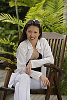 Woman sitting in garden, smiling at camera, portrait - Asia Images Group