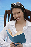Woman by swimming pool, reading a book - Asia Images Group