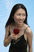 Woman holding a glass of wine, looking away, swimming pool in the background - Asia Images Group