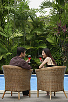 Couple sitting by swimming pool, drinking wine - Asia Images Group