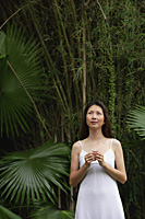 Woman standing outdoors, looking up, hands clasped - Asia Images Group