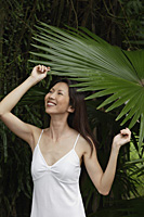 Woman in white top, standing under big leaf - Asia Images Group