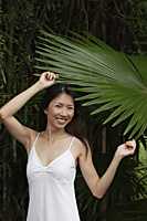 Woman in white top, standing under big leaf, smiling at camera - Asia Images Group