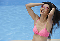 Woman in pink bikini, sitting by swimming pool, hands in hair, smiling - Asia Images Group