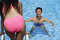 Man in swimming pool, smiling at woman standing in front of him - Asia Images Group