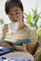 Woman sipping from cup, reading a book - Asia Images Group