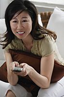 Woman holding TV remote control - Asia Images Group
