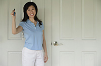 Woman standing next to door, holding house keys, smiling - Asia Images Group