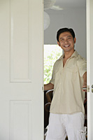 Man at home, standing at doorway, smiling - Asia Images Group