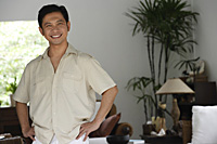Man standing in living room, hands on hips, smiling - Asia Images Group