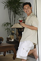 Man leaning against doorway, holding glass of wine - Asia Images Group