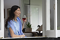 Woman at home, looking out of the window, holding wine glass - Asia Images Group
