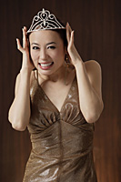 woman wearing crown, holding crown on head, smiling - Asia Images Group