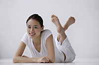 Woman lying on stomach on floor, looking at camera, smiling - Asia Images Group