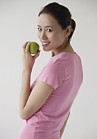 Woman looking over shoulder at camera, smiling, holding apple - Asia Images Group