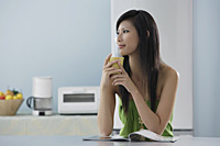 woman drinking out of mug in kitchen with magazine - Asia Images Group
